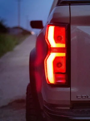Pickup truck rear taillight illuminated at dusk on a rural road